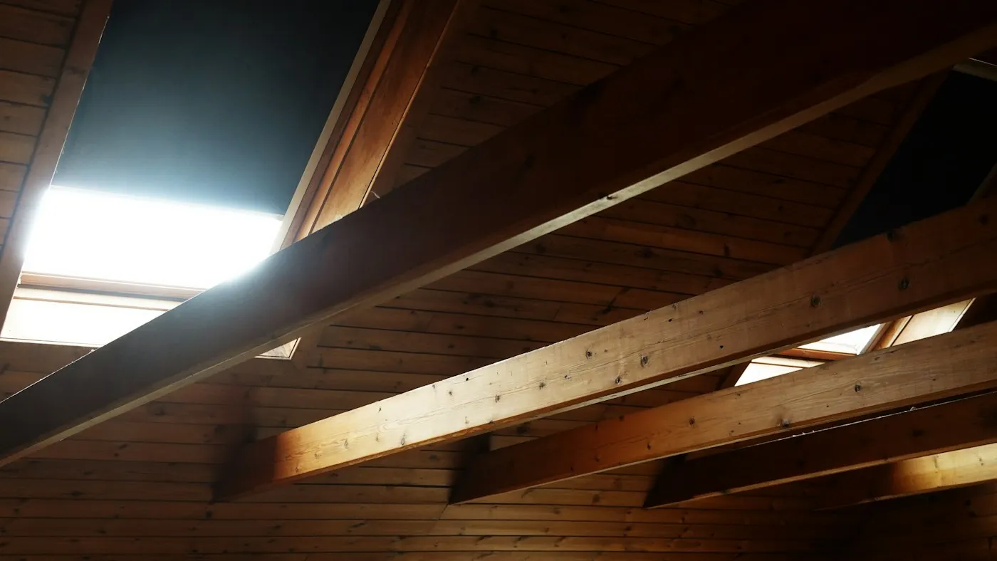 Sunlight through roof windows illuminating exposed wooden attic beams